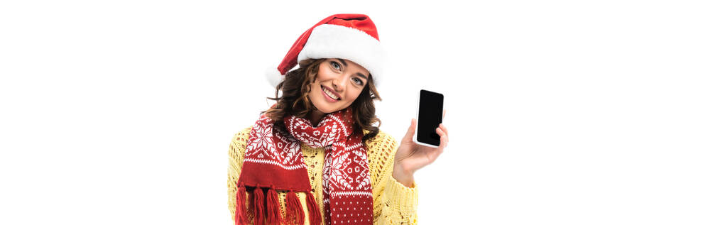 πανοραμική καλλιέργεια χαρούμενη νεαρή γυναίκα στο καπέλο Σάντα και κασκόλ κρατώντας smartphone με λευκή οθόνη απομονώνονται σε λευκό  - Φωτογραφία, εικόνα