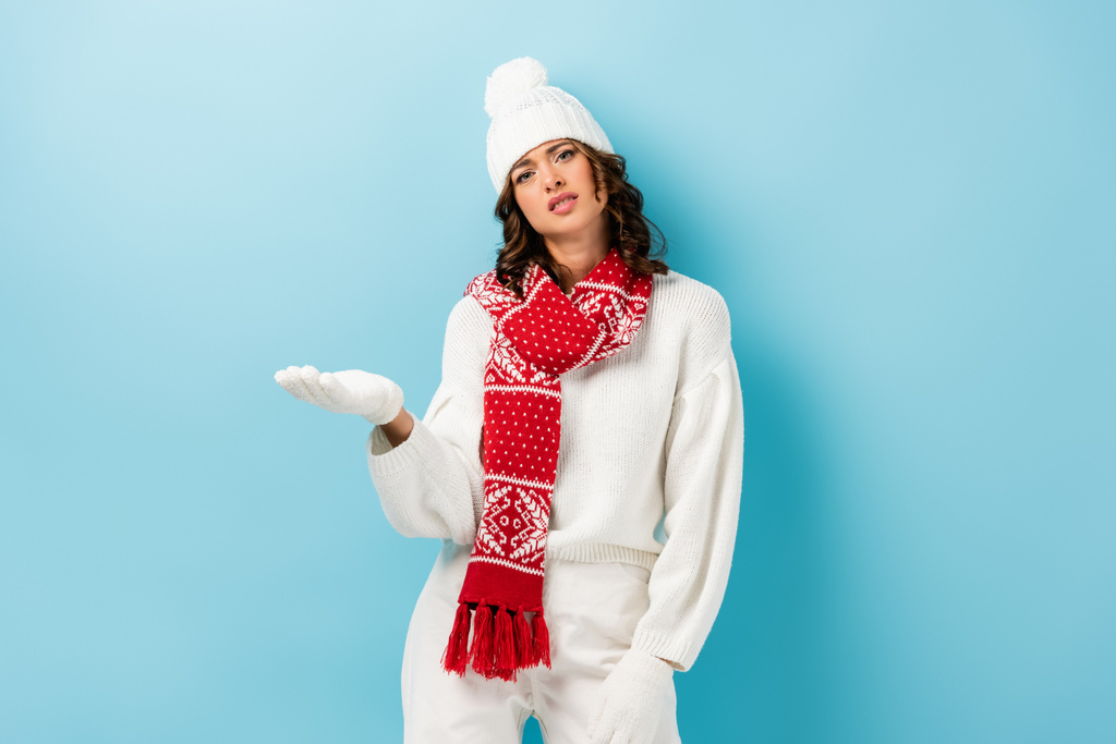 jeune femme mécontente en tenue d'hiver blanche pointant avec la main sur le bleu  - Photo, image