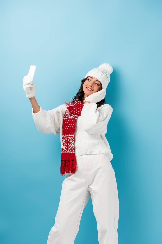 Beyaz kışlık kıyafetli, mutlu genç bir kadın mavi selfie çekiyor. - Fotoğraf, Görsel
