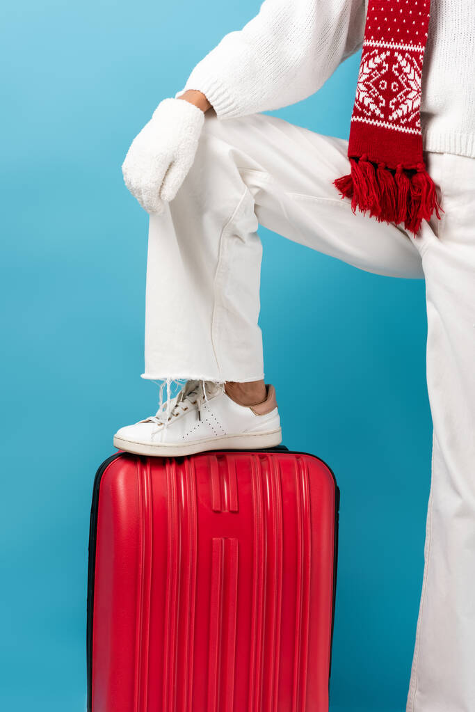 青いスーツケースに身を包んだ冬服姿の若い女性のクロップドビュー - 写真・画像