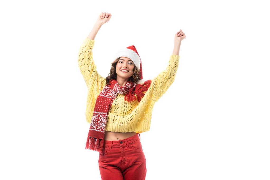 young happy woman in santa hat and red scarf standing with hands above head isolated on white  - Photo, Image