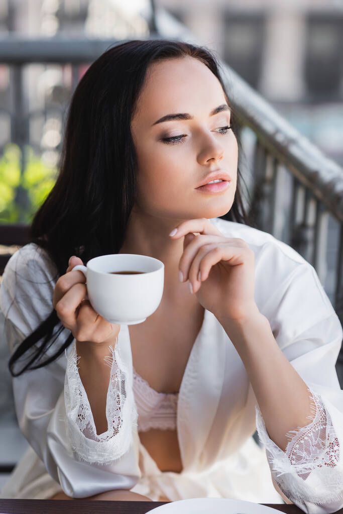 美しいブルネットの女性で白いローブバルコニーでコーヒーを飲む - 写真・画像