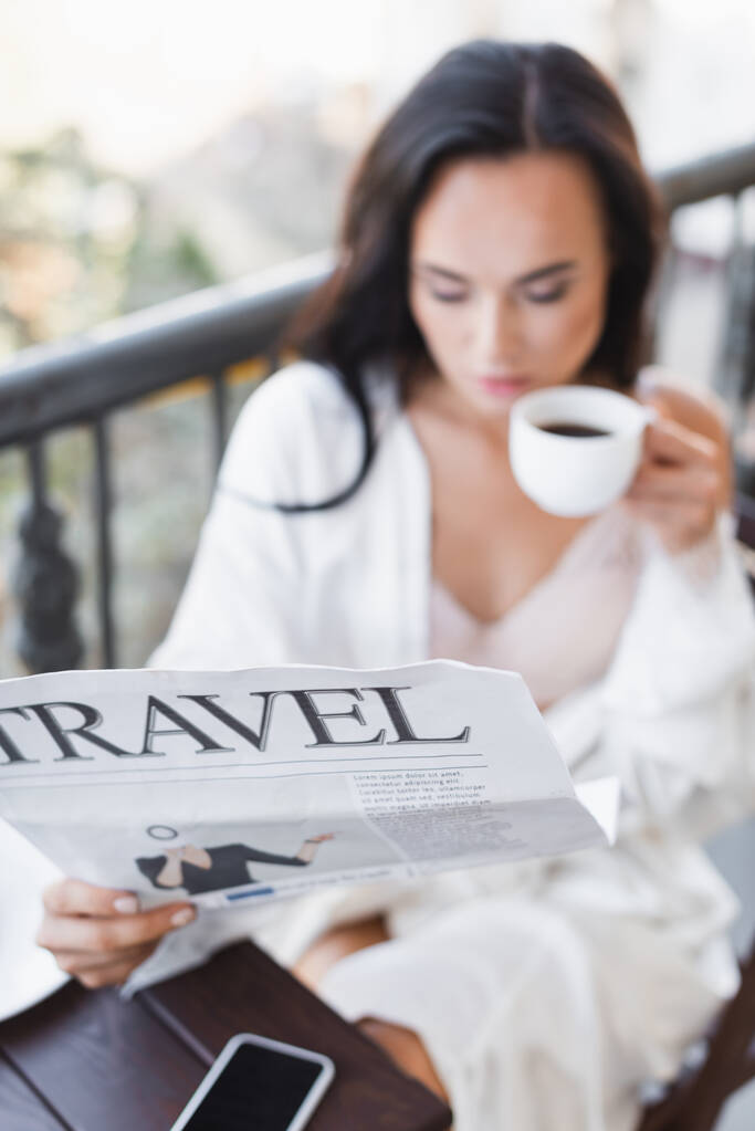 barna nő fehér köntösben ül az erkélyen és újságot olvas - Fotó, kép
