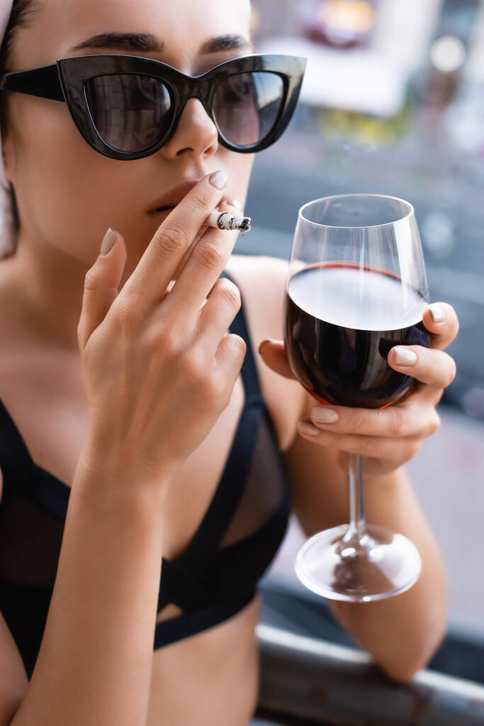 sexy jonge vrouw in zwart ondergoed roken sigaret en het drinken van wijn op balkon - Foto, afbeelding