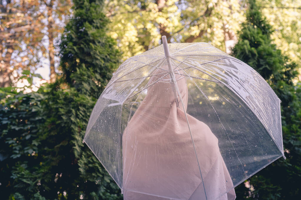 Otoño. Mujer solitaria musulmana en un pañuelo en la cabeza bajo un paraguas transparente con gotas de lluvia caminando en un parque, jardín. Paisaje lluvioso. Tonificado Vintage - Foto, Imagen