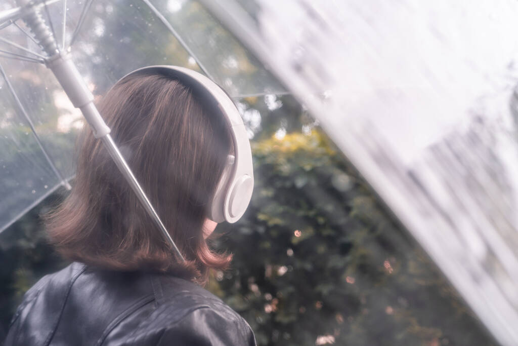 Sonbahar. Parkta yürüyen, kulaklıklı yalnız, üzgün bir kadın. Islak şeffaf şemsiyeden yağmur damlalarıyla bak. Yağmurlu bir manzara. Vintage Tone - Fotoğraf, Görsel