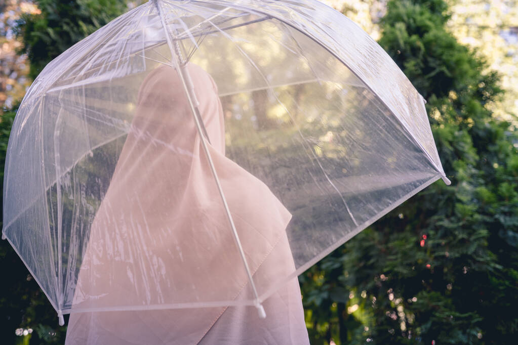 Sonbahar. Şeffaf bir şemsiyenin altında başörtüsü takan yalnız Müslüman bir kadın. Parkta, bahçede yağmur damlaları geziyor. Yağmurlu bir manzara. Vintage Tone - Fotoğraf, Görsel