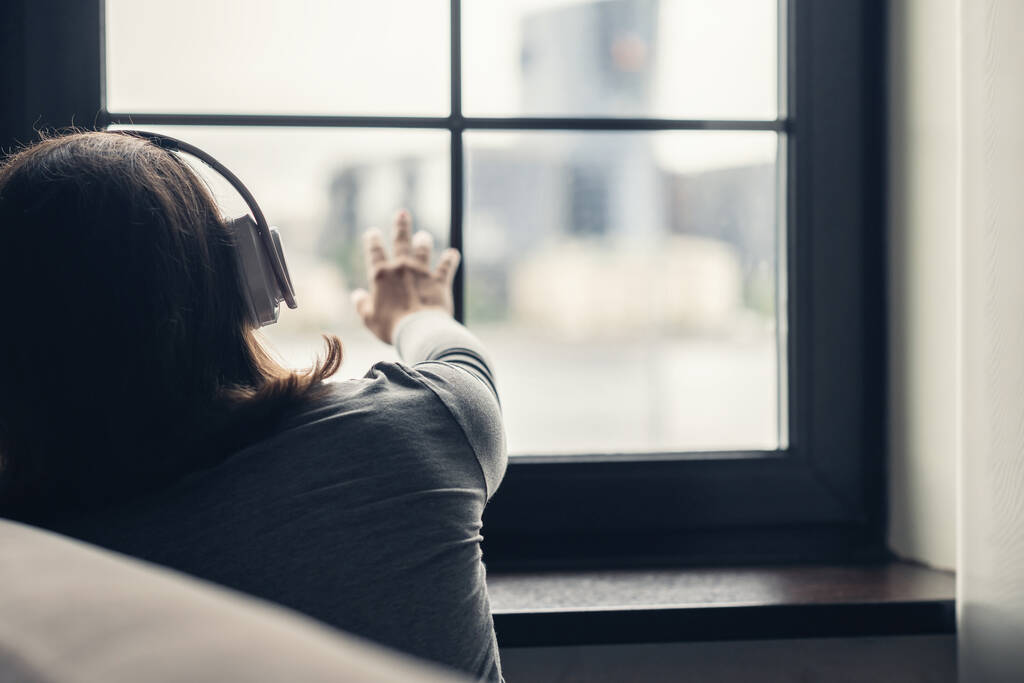 Vista trasera de mujer morena solitaria en auriculares escuchar música y tocar ventana. Concepto - Foto, Imagen