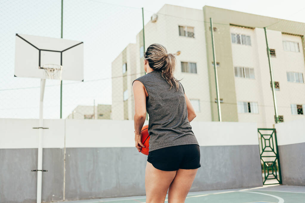 Nuori latino nainen urheiluvaatteet pelaa koripalloa ulkona kentällä - Valokuva, kuva