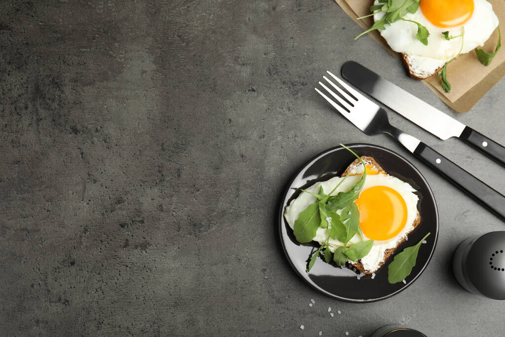 Πεντανόστιμο σάντουιτς με ρόκα και τηγανητό αυγό σε γκρι τραπέζι, επίπεδο κρεβάτι. Χώρος για κείμενο - Φωτογραφία, εικόνα