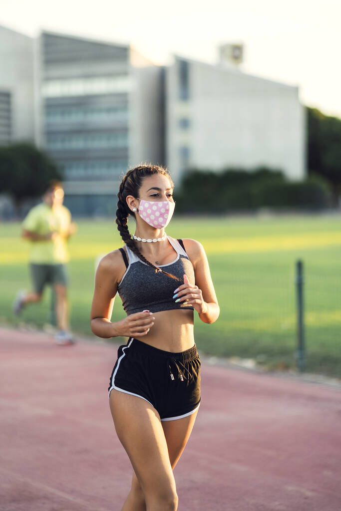 Tıbbi koruyucu maske takan genç bir atletik kadın koşucu. - Fotoğraf, Görsel