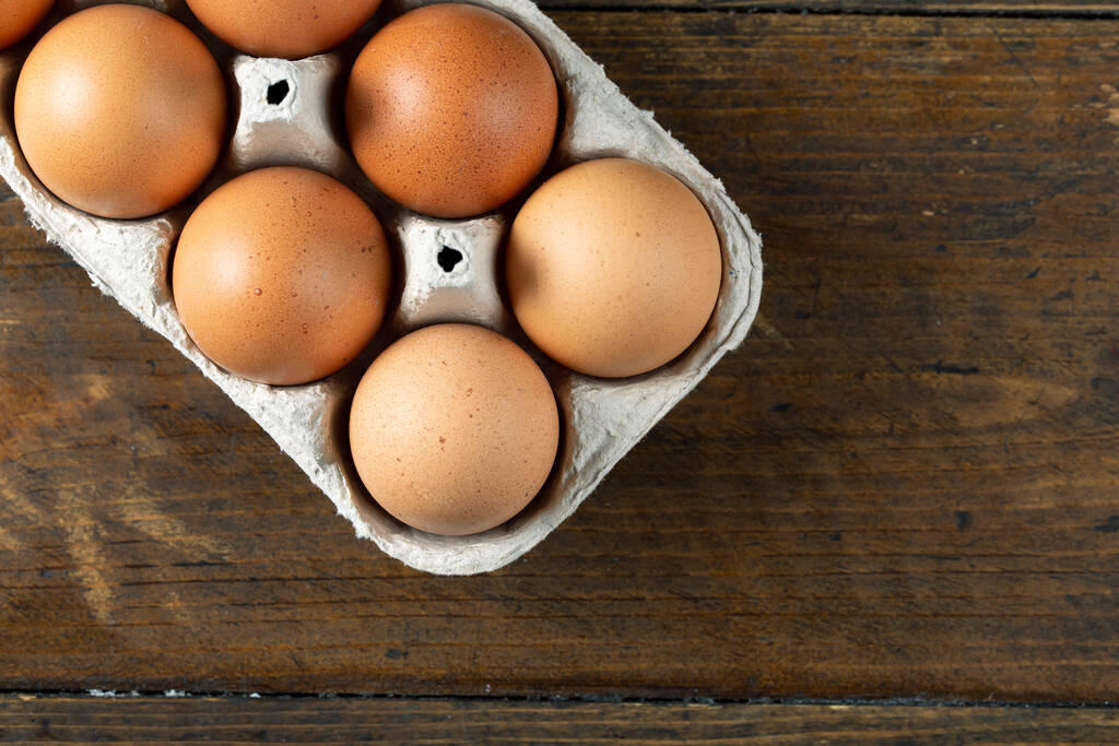 Huevos de pollo en un cartón de huevo abierto sobre fondo de madera. Vista superior con espacio de copia. Concepto natural de alimentación saludable y agricultura ecológica.  - Foto, Imagen
