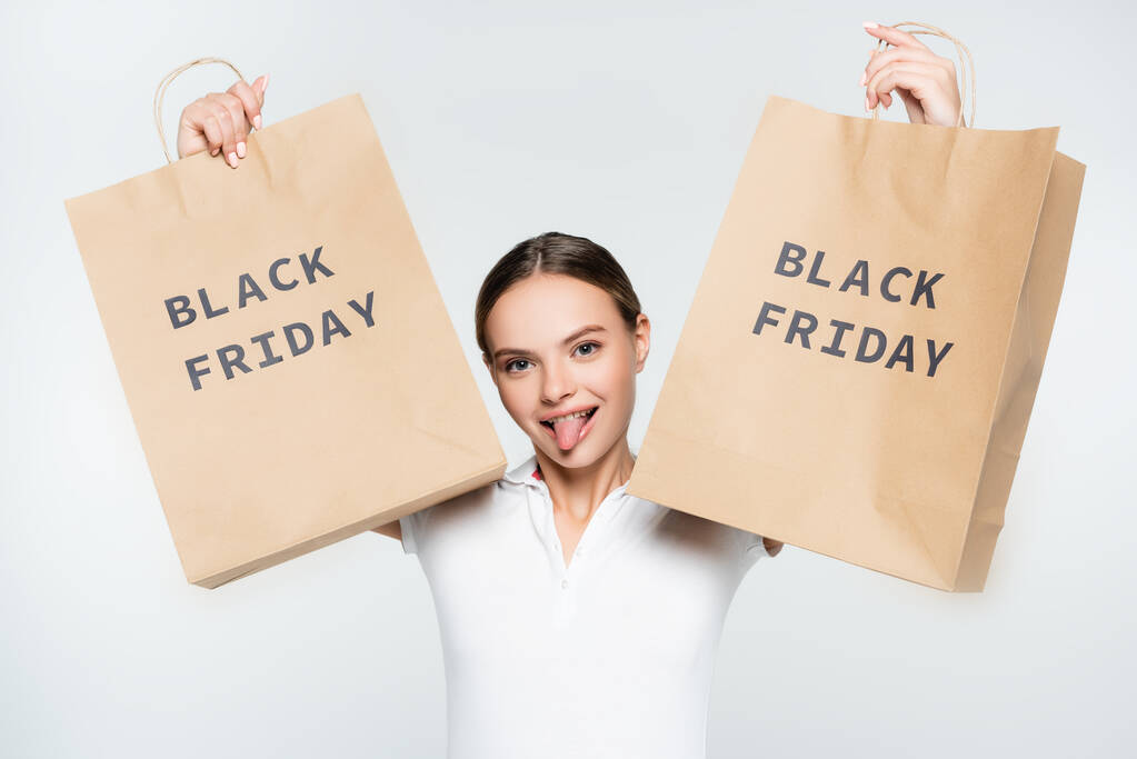junge Frau streckt Zunge heraus und hält Einkaufstüten mit schwarzem Freitag-Schriftzug auf weißem Grund - Foto, Bild
