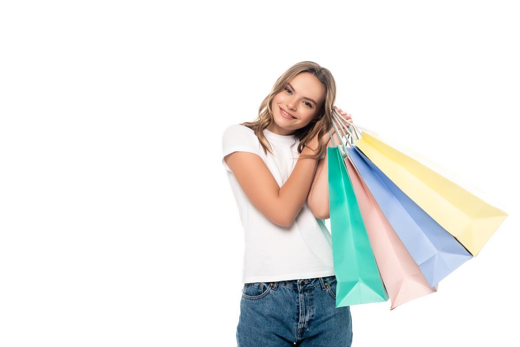 Genç bir kadın renkli alışveriş torbaları tutuyor ve beyaza izole edilmiş kameraya bakıyor. - Fotoğraf, Görsel