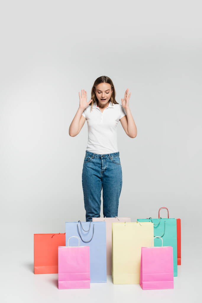 jovem mulher animado gesticulando enquanto olha para sacos de compras no conceito cinza, preto sexta-feira  - Foto, Imagem