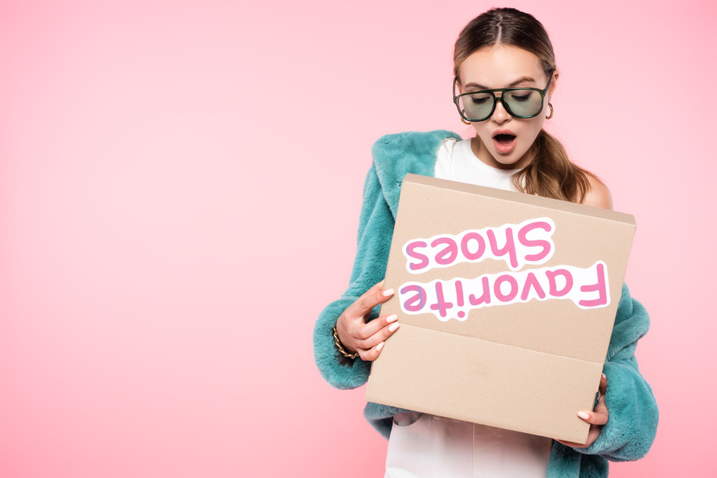 shocked woman in sunglasses looking at box with favorite shoes lettering on pink, black friday concept - Photo, Image
