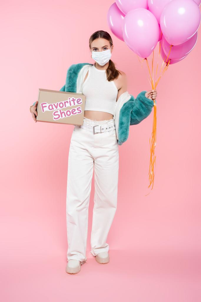 jovem mulher em máscara médica segurando caixa com sapatos favoritos lettering e balões em rosa  - Foto, Imagem