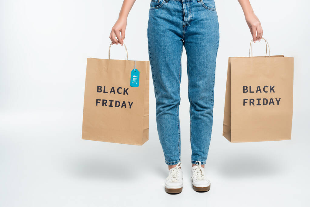 vista recortada de los clientes sosteniendo bolsas de compras con etiqueta de venta y letras de viernes negro en blanco  - Foto, imagen