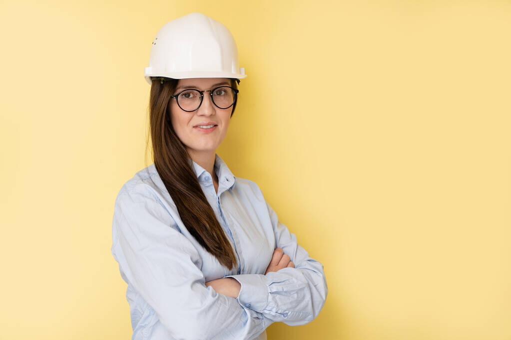 Portrait of smiling beautiful tatar woman engineer in construction helmet and glasses isolated on yellow background - Photo, Image