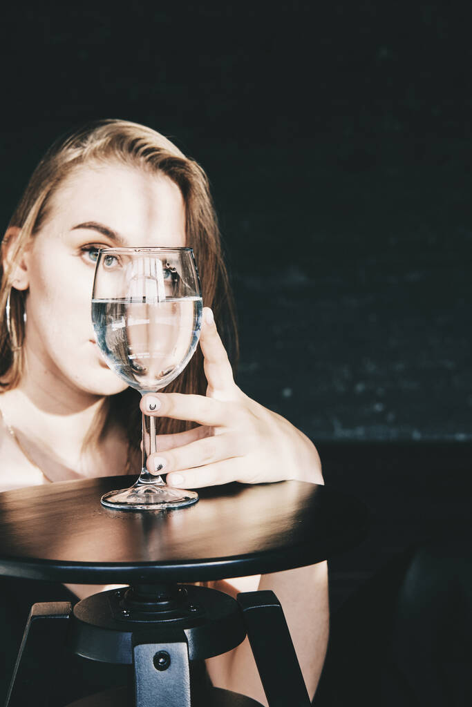mulher olhando através do copo de vinho ou água sob luz dura. - Foto, Imagem