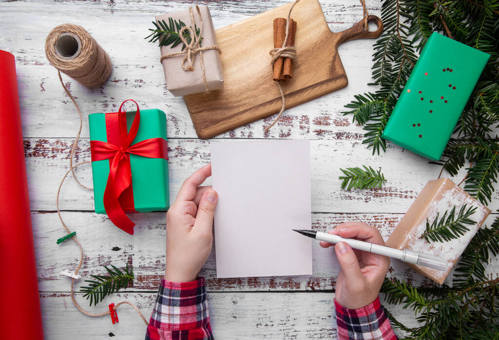 Eller masanın üzerinde hediyelerin yanında bir kalem ve kartpostal tutar. - Fotoğraf, Görsel