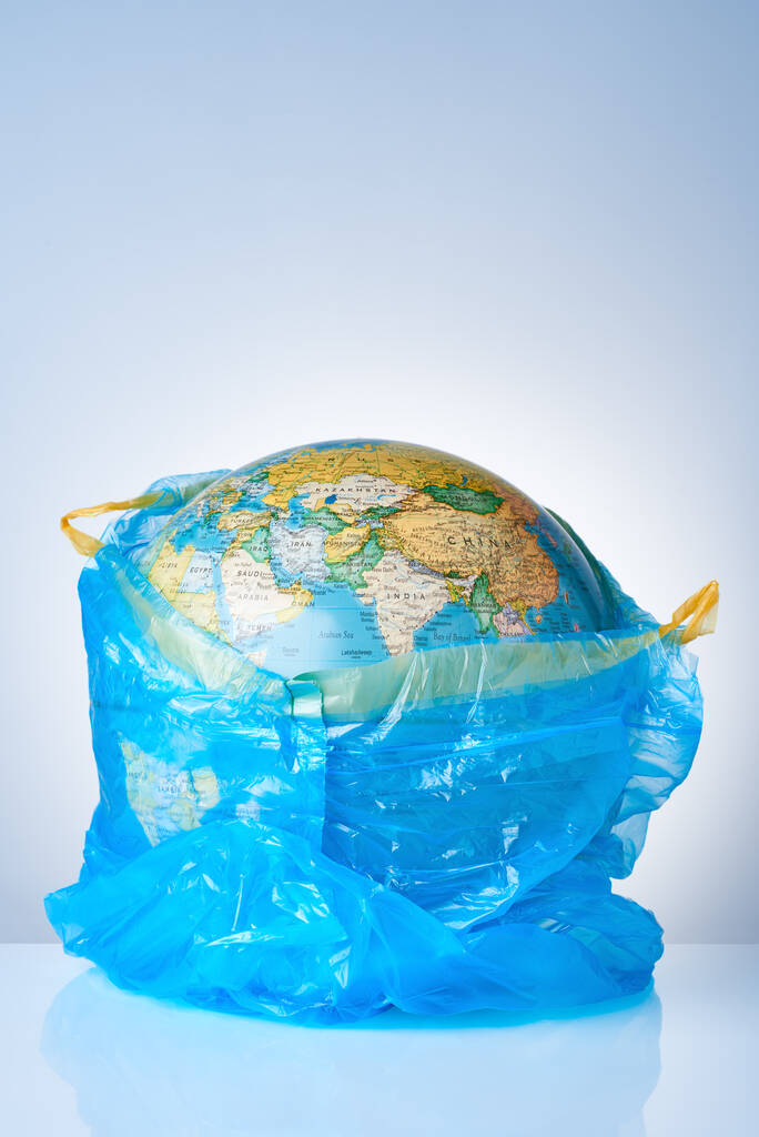 Das Konzept, die Welt vor Plastikmüll zu schützen, gegen Umweltverschmutzung zu kämpfen, für die Umwelt zu kämpfen, eine Erdkugel in einem blauen Müllsack auf hellem Hintergrund. Keine Plastiktüten - Foto, Bild