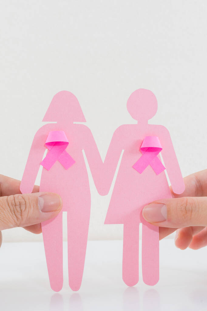 Un plan vertical de mains féminines tenant des filles en papier avec ruban rose comme symbole de sensibilisation au cancer du sein - Photo, image