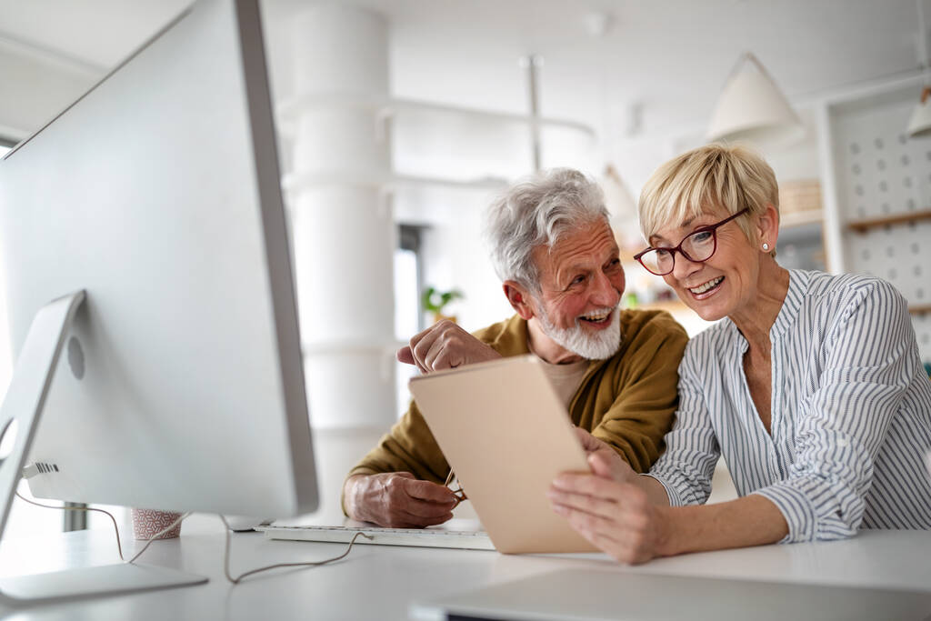 Весела щаслива старша пара використовує технологічні пристрої і розважається вдома
 - Фото, зображення
