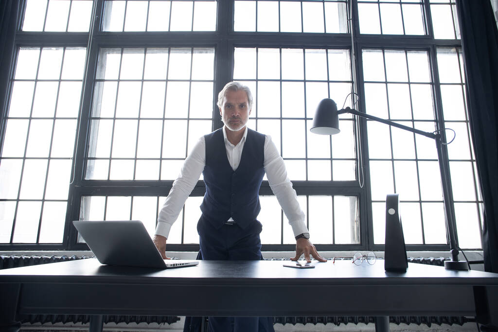 Confident businessman posing leaning on a table in an office. - Photo, Image