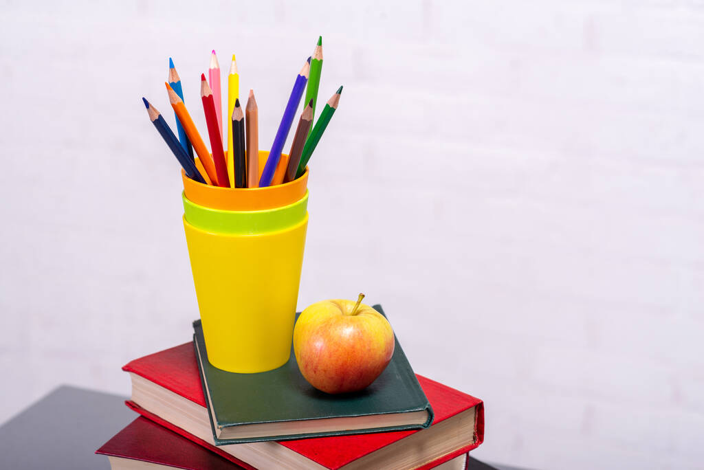 A stack of books and a glass with pencils on the table close-up. School supplies. - Photo, Image