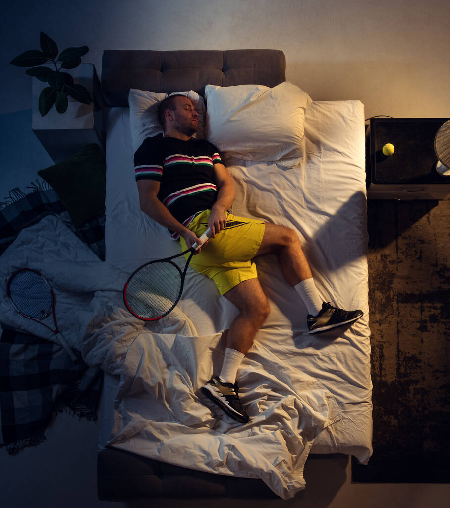 Вид зверху молодого професійного тенісиста, який спить у своїй спальні в спортивному одязі з ракеткою
 - Фото, зображення