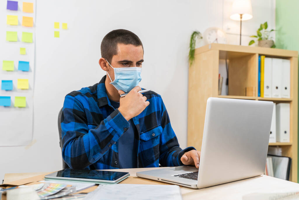 Casual business man in startup office working on laptop with face mask because coronavirus. Business man with post it stickers background. Creative studio. Man in modern office. - Photo, Image