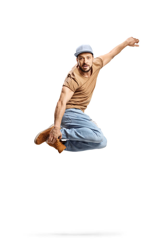 Full length shot of a guy with a cap jupming and holding his legs isolated on white background - Photo, Image
