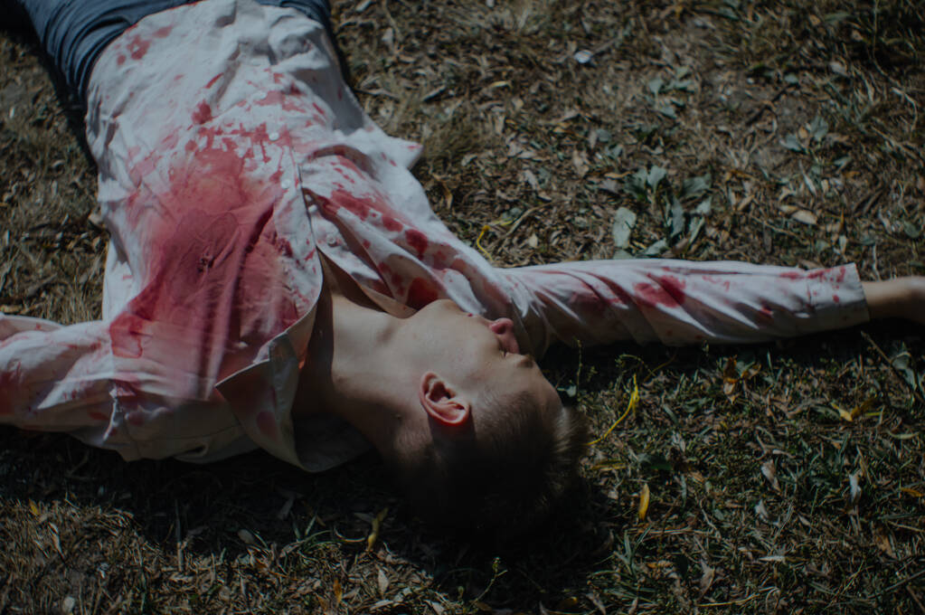 Тело мертвеца лежит на земле в окровавленной рубашке - Фото, изображение