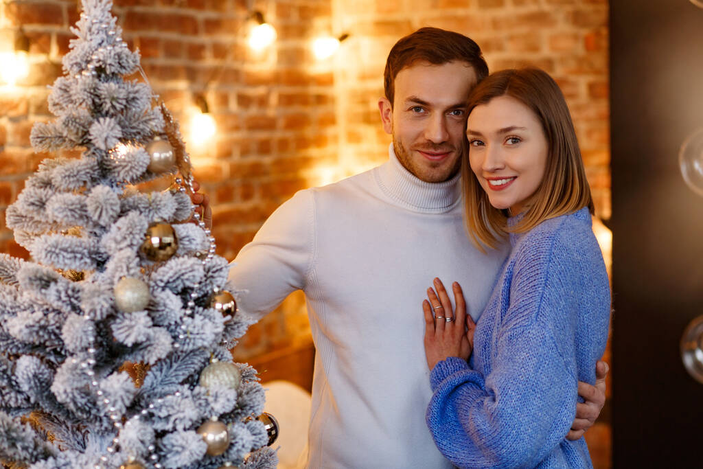 Hermosa pareja joven en casa decorando un árbol de Navidad. Pasar tiempo juntos, las relaciones y el concepto de personas. Vacaciones de invierno, celebraciones de Navidad, concepto de Año Nuevo - Foto, Imagen
