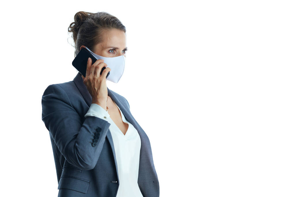 Δουλειές κατά τη διάρκεια πανδημίας κορωνοϊού. νεαρή γυναίκα σε γκρι κοστούμι με ιατρική μάσκα κοιτάζοντας την απόσταση που απομονώνεται σε λευκό φόντο. - Φωτογραφία, εικόνα