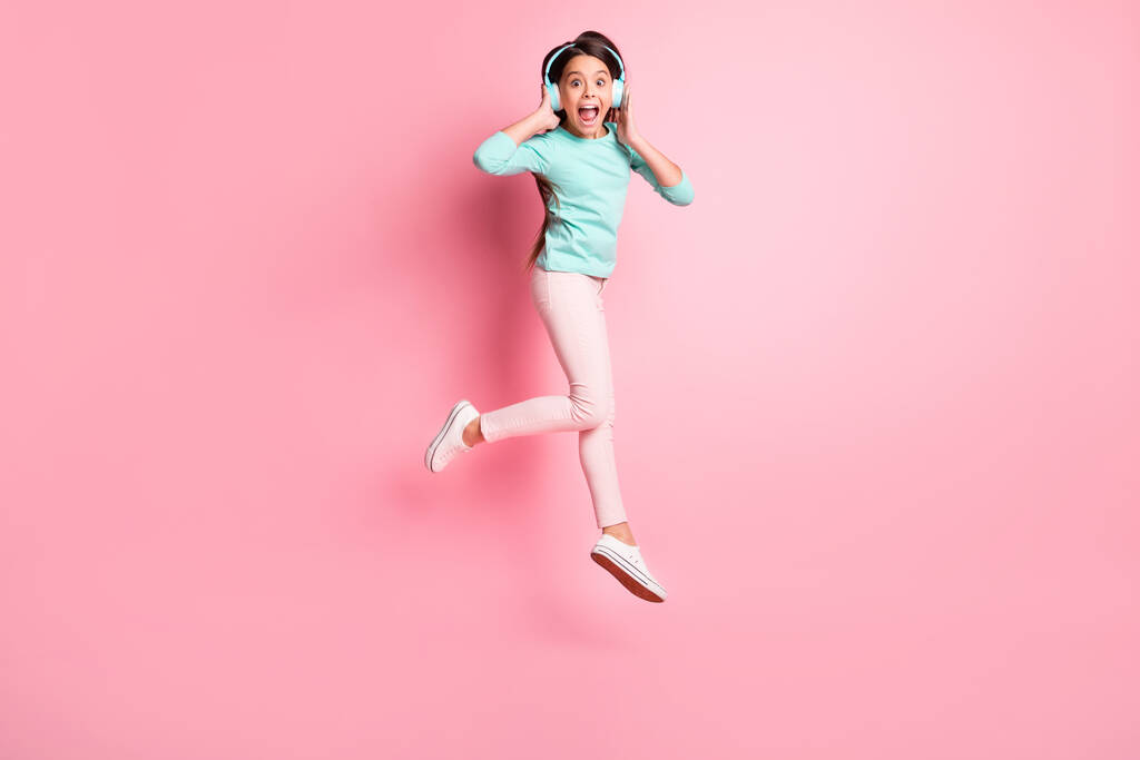 Фотографія повного розміру тіла божевільної маленької іспаномовної дівчинки, що стрибає вгору з криками в навушниках ізольовано на рожевому кольоровому фоні
 - Фото, зображення