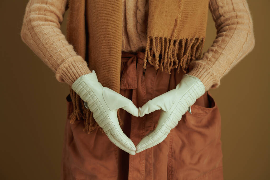 Hello autumn. Closeup on middle aged woman in scarf with leather gloves showing heart shaped hands isolated on beige background. - Photo, Image