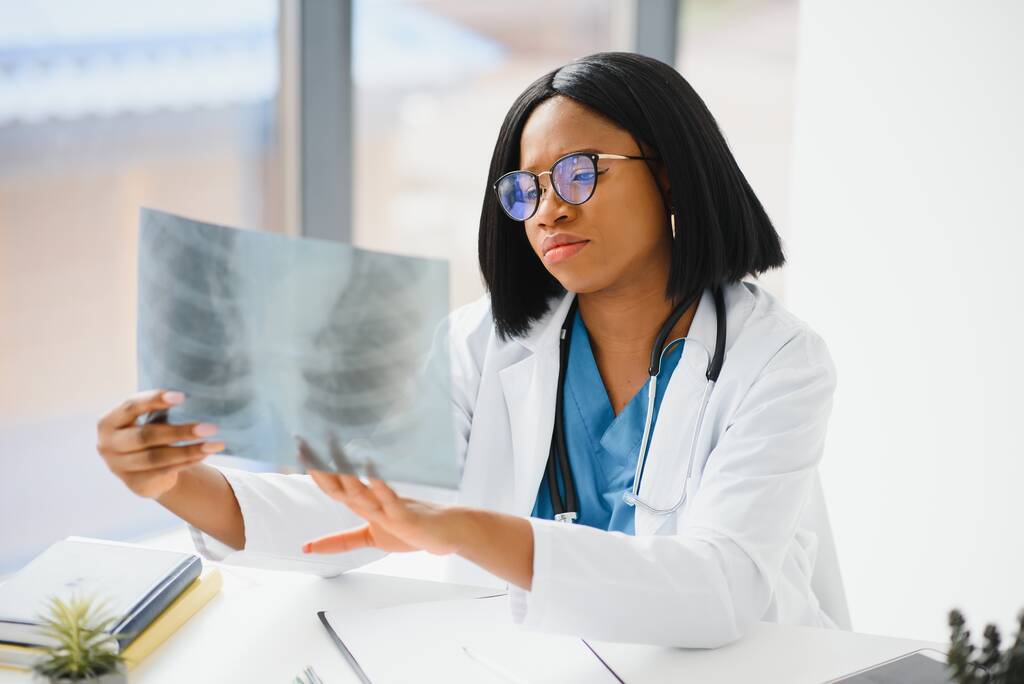 患者の胸部のX線を調べる若いプロのアフリカ系アメリカ人医師 - 写真・画像