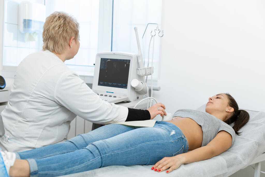 Il medico effettua una diagnosi ecografica dei pazienti addome e organi interni. Una ragazza giace su un divano in una sala diagnostica ad ultrasuoni. - Foto, immagini