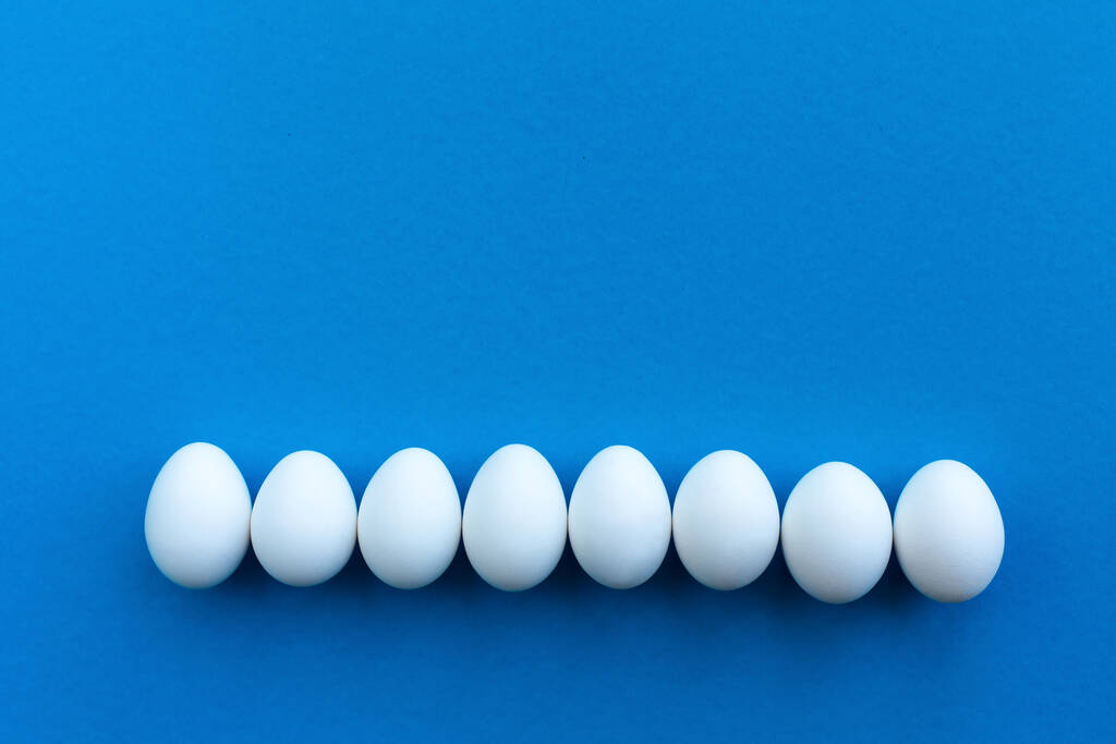 Λευκά αυγά κότας σε μπλε φόντο με μια γραμμή. Υγιεινά βιολογικά τρόφιμα και διατροφή έννοια. Θέμα Πάσχα. - Φωτογραφία, εικόνα