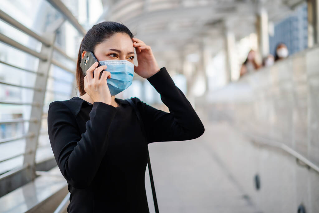 stresovaná žena nosí lékařskou masku a mluví s mobilním telefonem o svém obchodním problému, ochraně před pandemií koronaviru (covid-19) - Fotografie, Obrázek