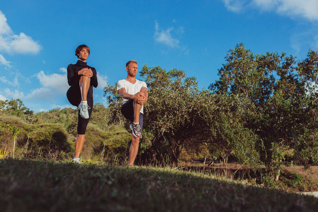 athletic young man and woman in sportswear warming up in park - Photo, Image