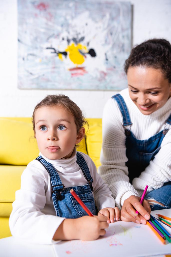 Дівчина стоїть біля матері і малює кольоровим олівцем на папері вдома
  - Фото, зображення