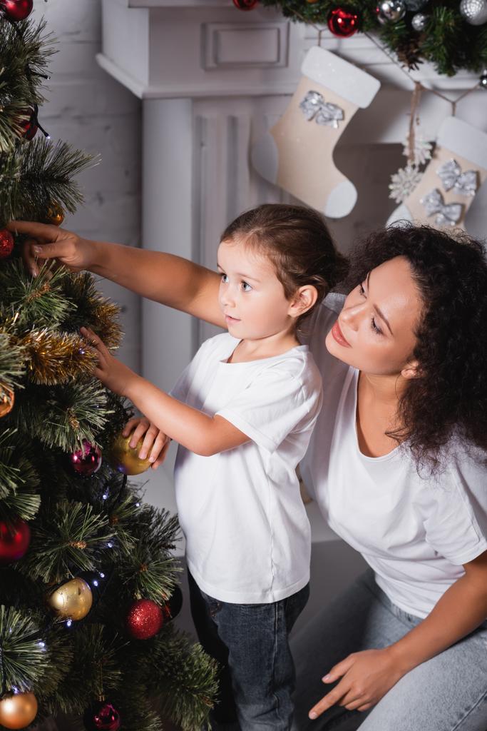 Madre e hija decorando pino de Navidad cerca de la chimenea en casa - Foto, Imagen