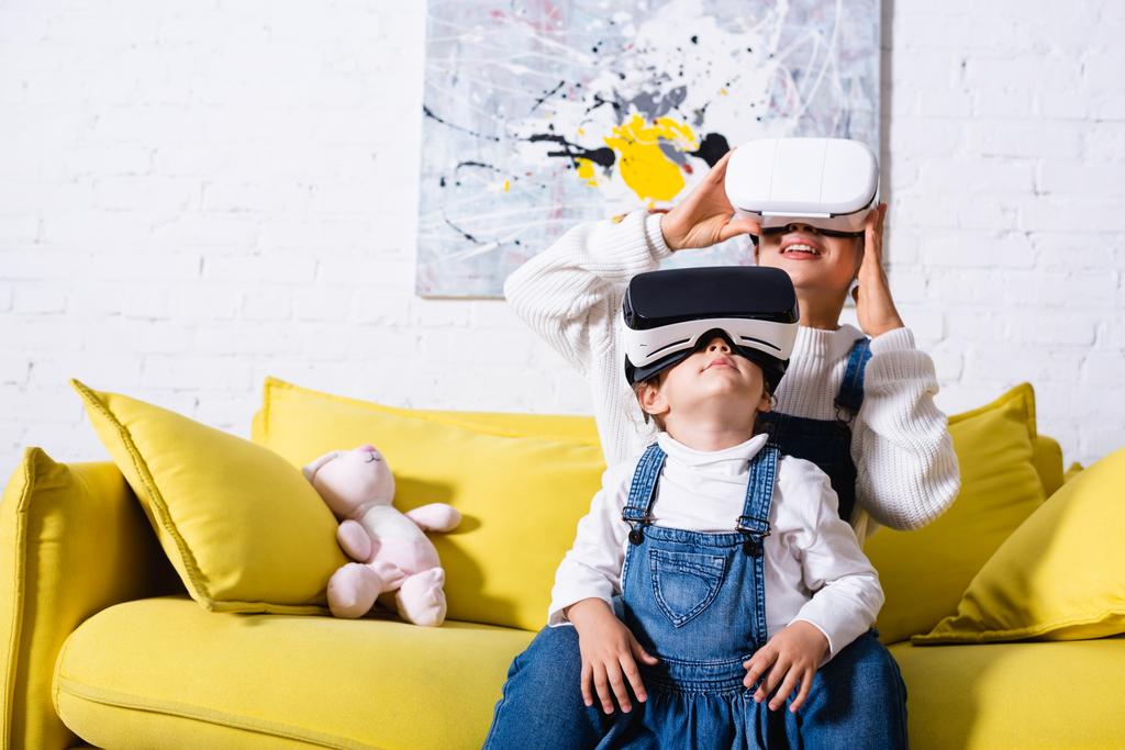  Daughter standing near mother in virtual reality headset at home - 写真・画像