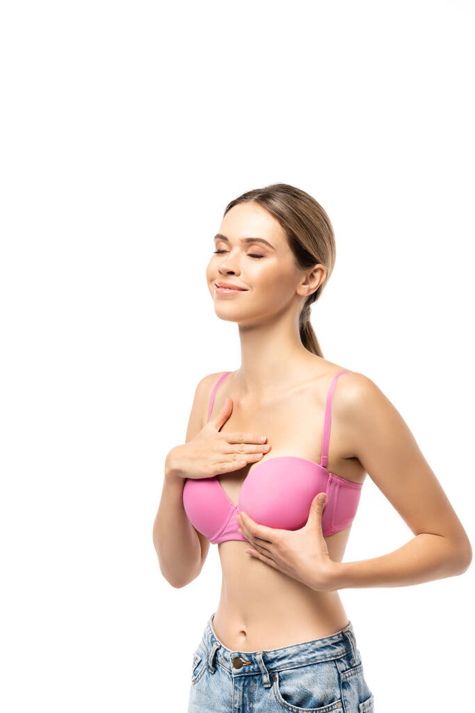 Jeune femme aux yeux fermés touchant le sein en soutien-gorge rose isolé sur blanc - Photo, image