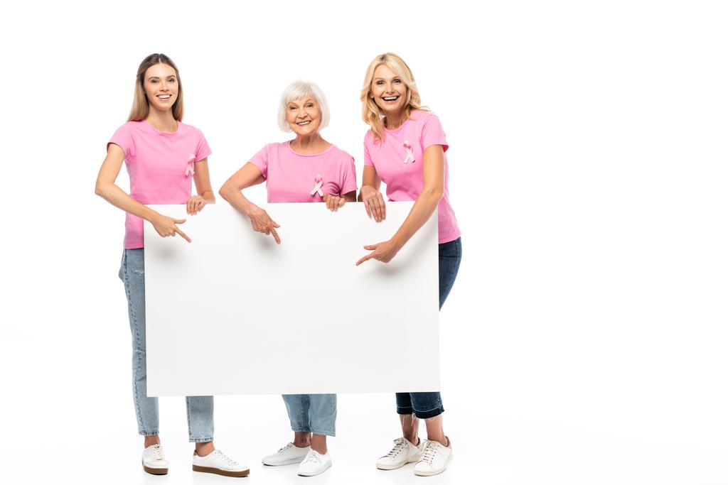 Женщины с розовыми лентами осведомлённости о раке молочной железы на футболках указывают на пустую доску на белом фоне - Фото, изображение