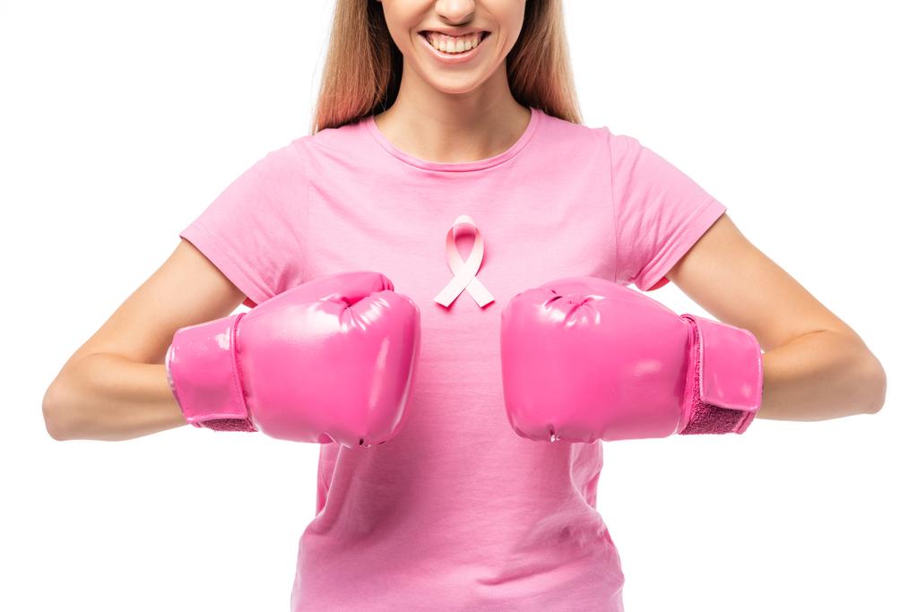Vista recortada de mujer joven con cinta rosa en camiseta y guantes de boxeo aislados en blanco - Foto, Imagen