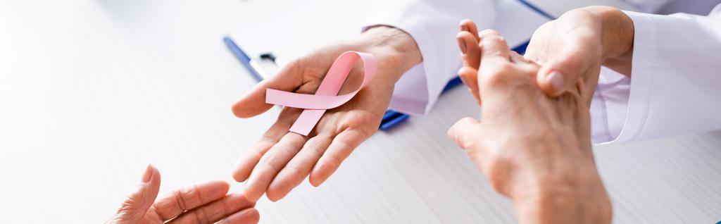 Panoramaaufnahme eines Arztes, der Patientenhände hält und rosafarbene Schleifen zeigt  - Foto, Bild